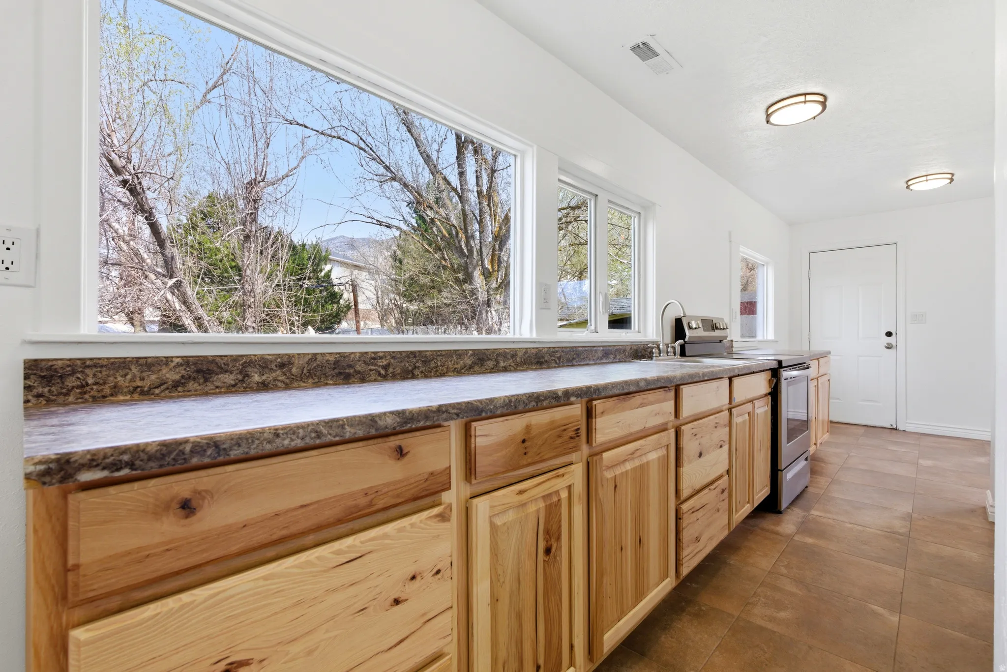 Kitchen featuring dark countertops, stainless steel electric stove, and light wood finish cabinetry