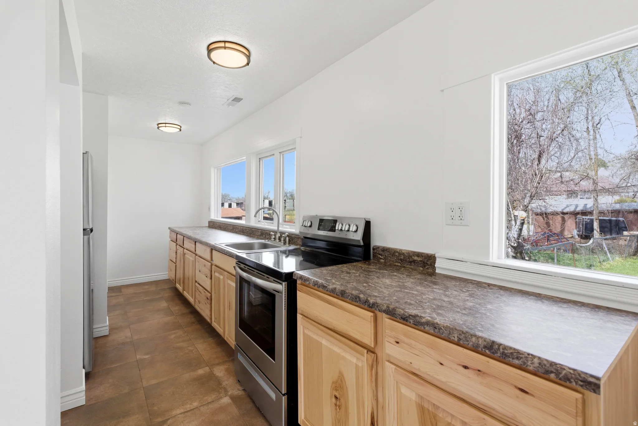 Kitchen with stainless steel appliances, dark countertops, and light wood finish cabinetry