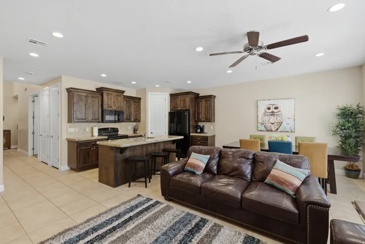 Open-concept living space featuring wood-finish cabinetry, a breakfast bar with stone-finish countertop, recessed lighting, and tile flooring