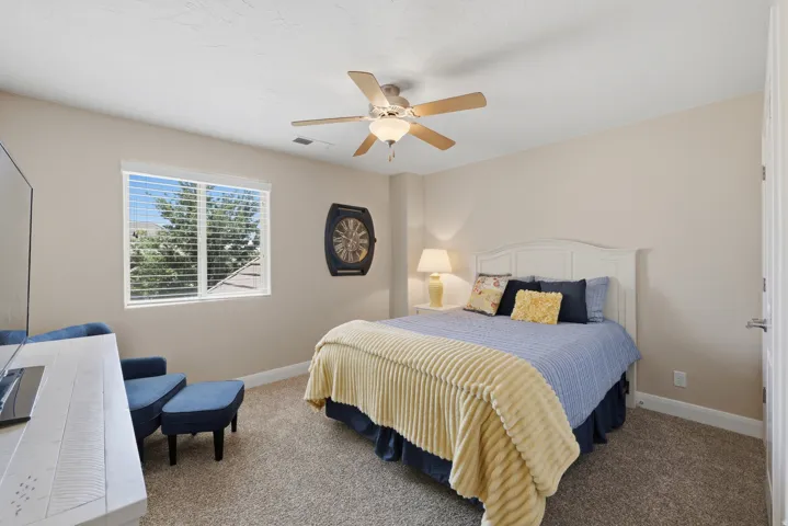 Bedroom featuring a window with horizontal blinds, a white headboard, a ceiling fan with integrated lighting, and carpeted flooring