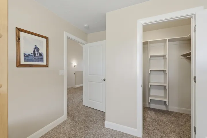 Hallway featuring light-toned walls, contrasting white trim, and textured carpet flooring