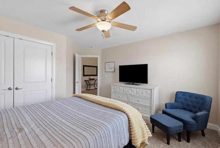 Bedroom featuring light neutral wall tones, carpeted flooring, a ceiling fan with integrated lighting, and white bi-fold closet doors with brushed nickel hardware