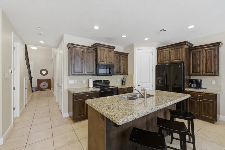 Kitchen featuring dark wood cabinetry, light granite countertops, a large island with an undermount double sink, and tile flooring