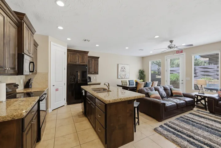 Open concept living area featuring a kitchen with granite countertops, rich wood cabinetry, and a central island with a double basin sink