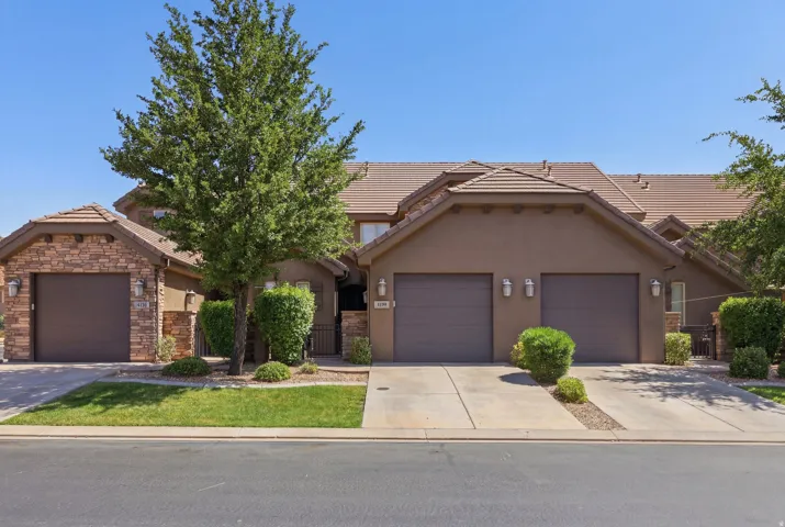 Exterior featuring a stucco and stone facade, tile roofing, multiple garage doors, concrete driveways, and mature landscaping