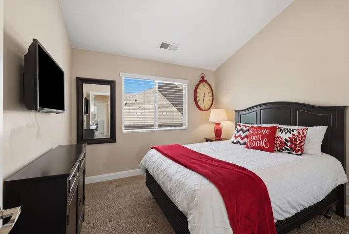 Carpeted bedroom with a window featuring horizontal blinds, a mounted television, and a dark wood dresser
