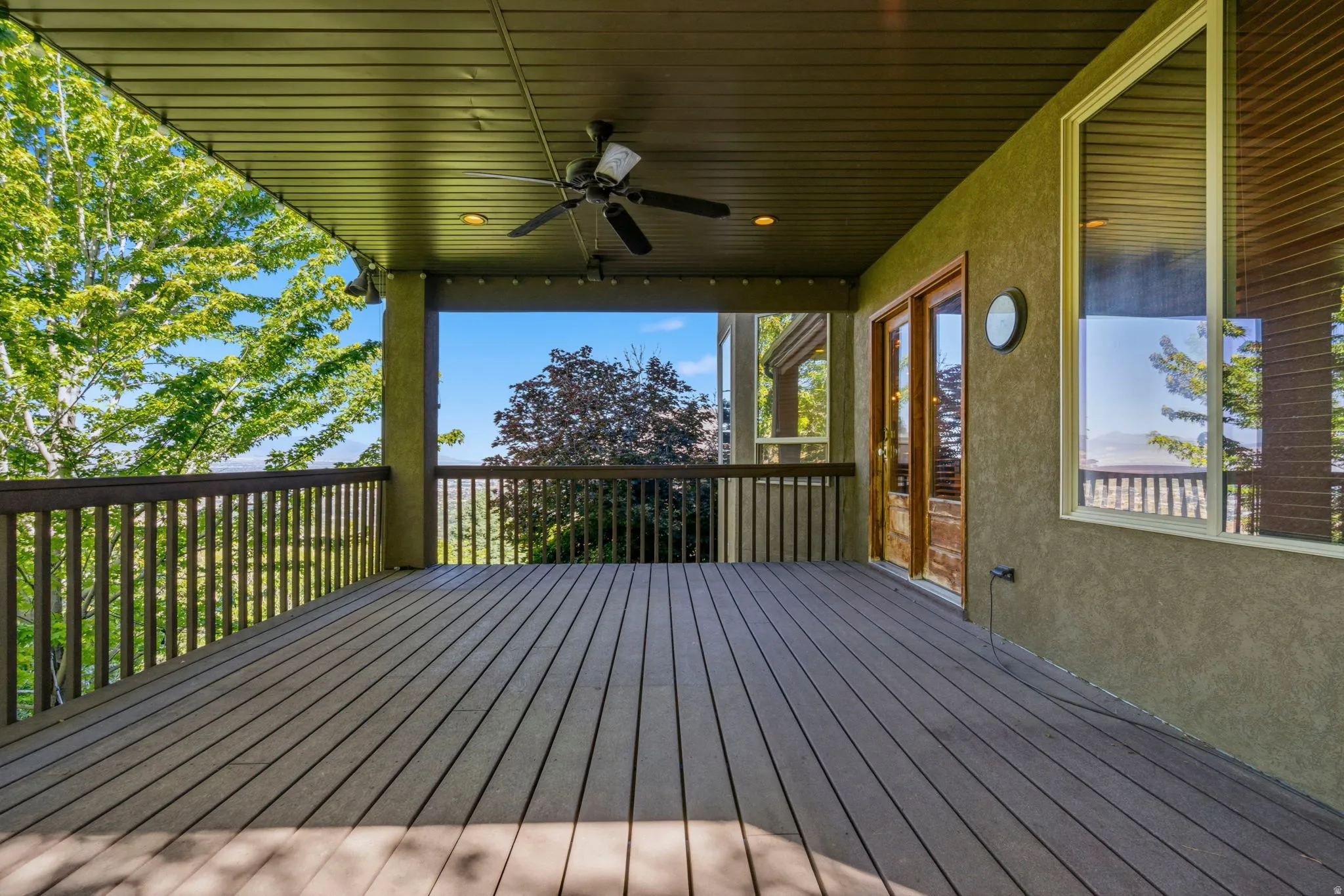 Spacious covered deck featuring composite decking, dark wood railing, and a ceiling fan with integrated lighting