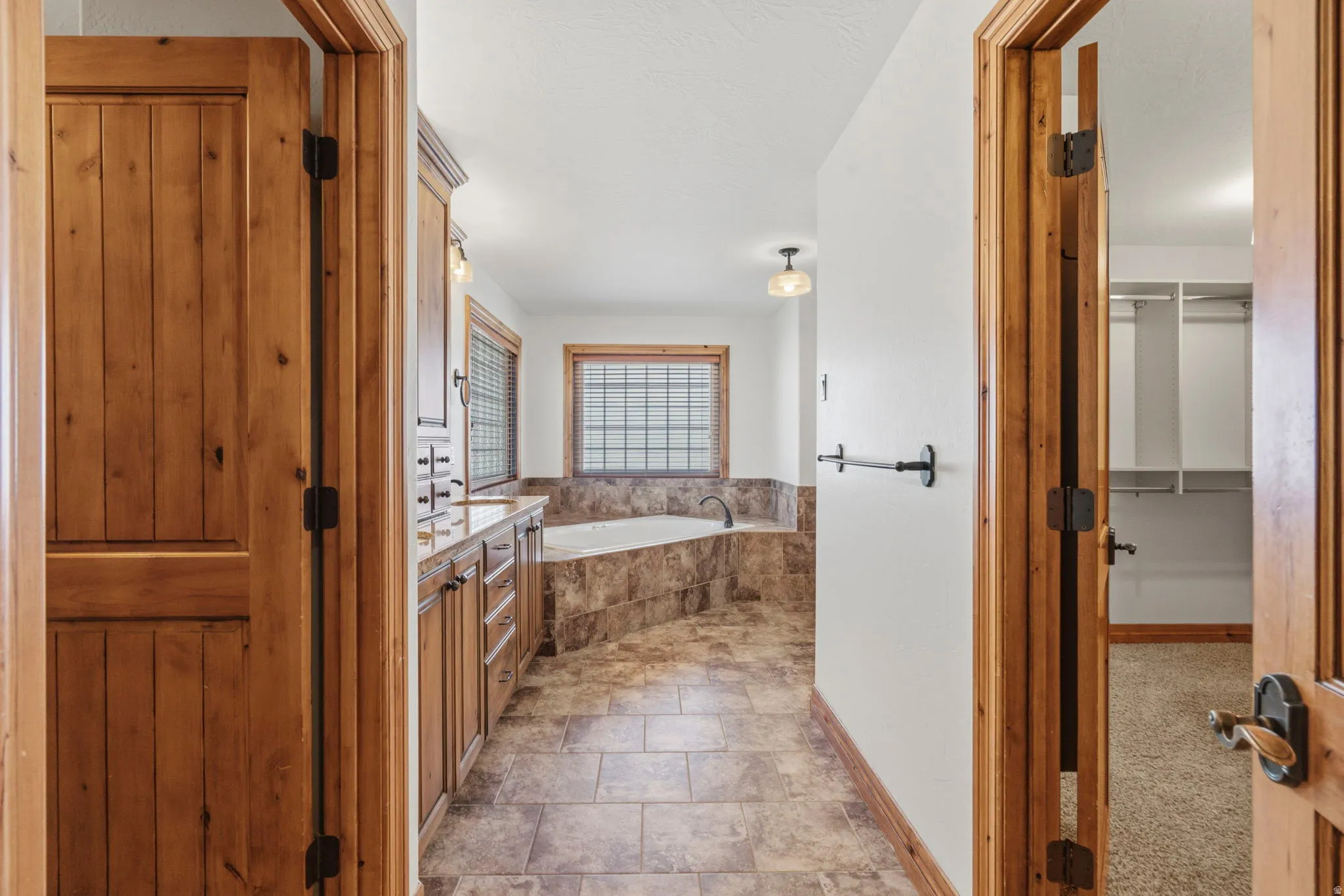 Primary en suite Bathroom featuring a built-in jetted tub with tile surround, wood-finish vanity with countertop, tile flooring