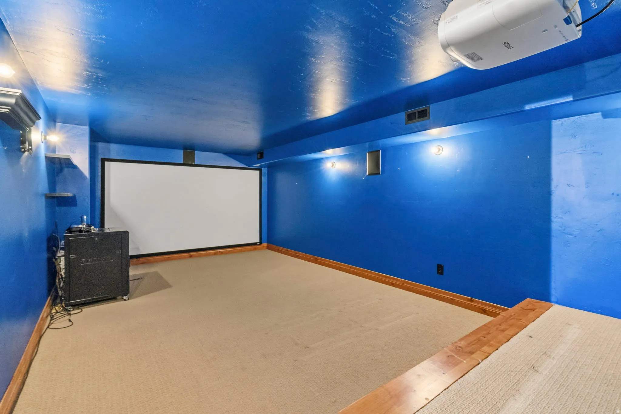 Dedicated entertainment space featuring a large projection screen, wall-mounted projector, and sconce lighting