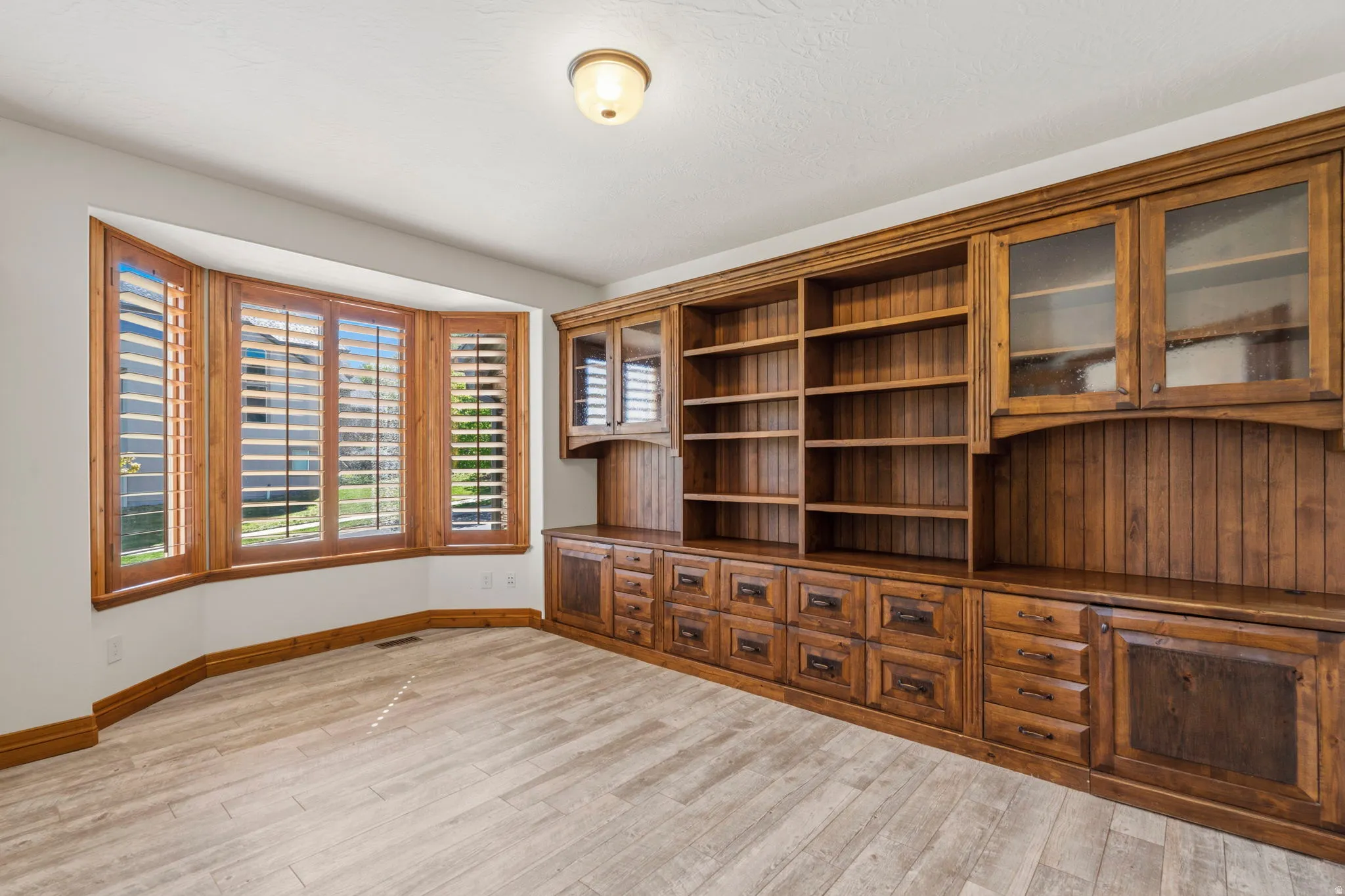 Built-in wood cabinetry with glass-front uppers and ample drawer storage, complemented by a bay window with wood-finish plantation shutters
