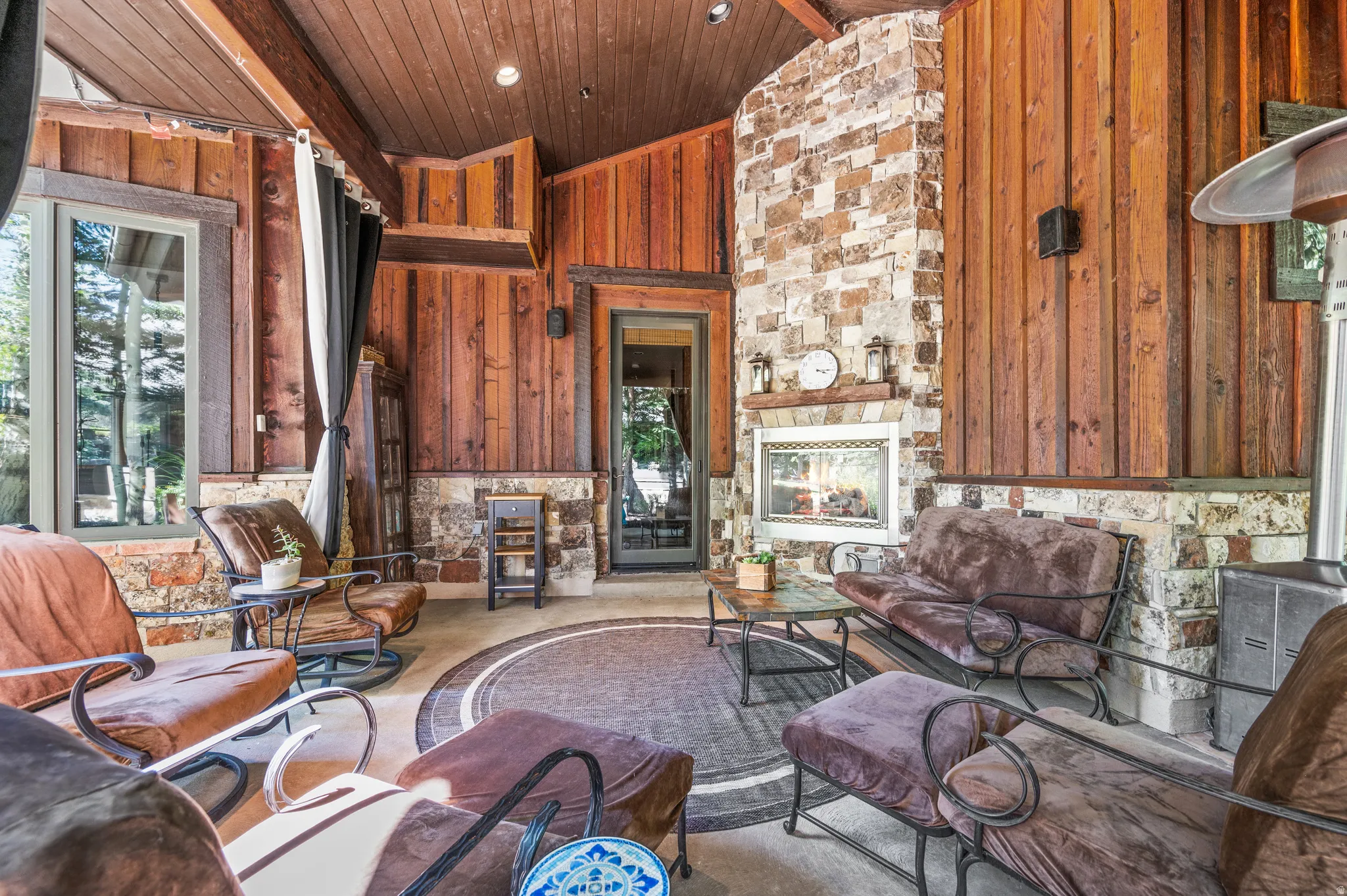 Living area with an outdoor stone fireplace, wood walls, recessed lighting, and a vaulted wood ceiling
