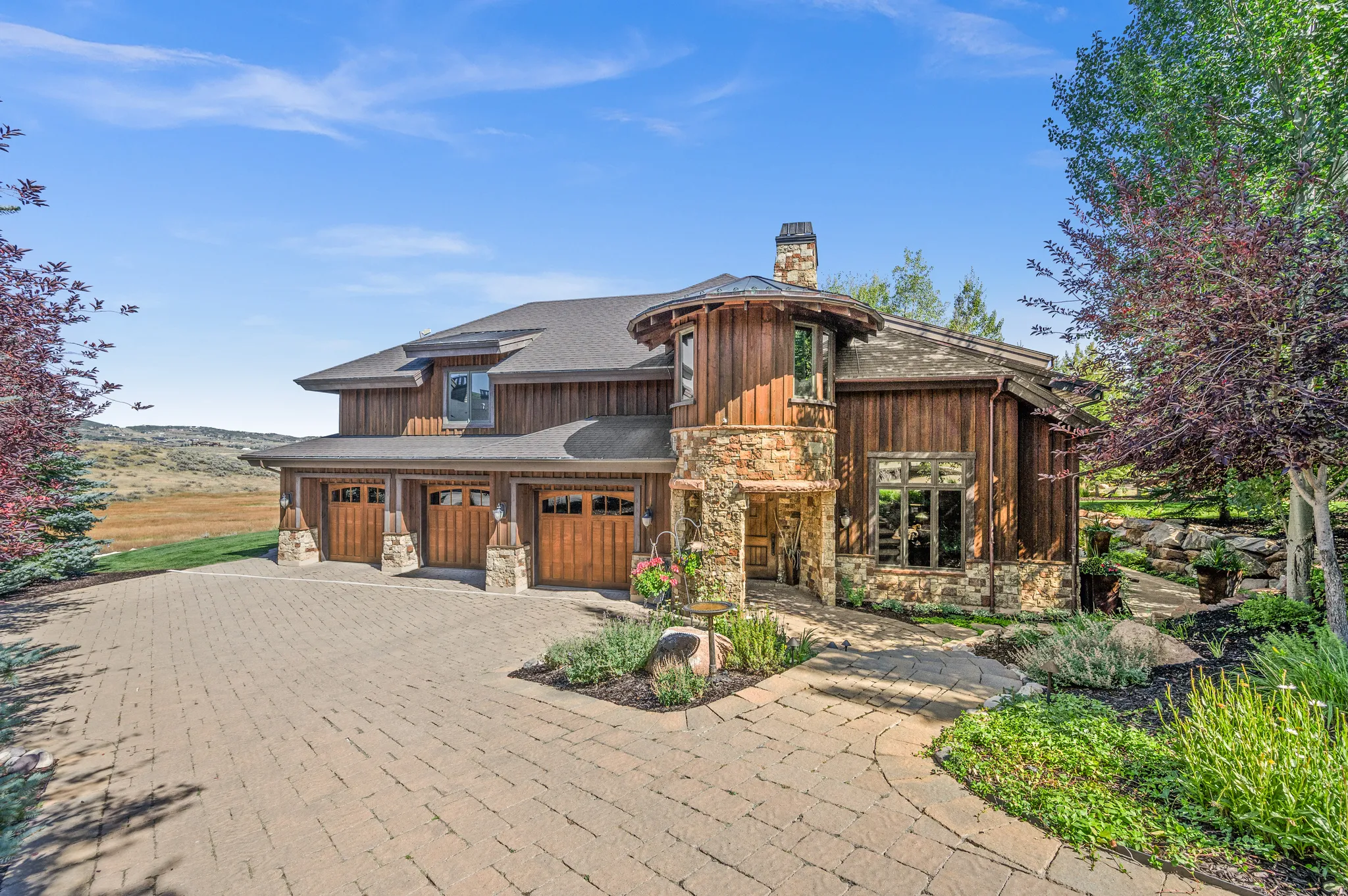 Rustic home with stone siding, decorative driveway, roof with shingles, and a chimney