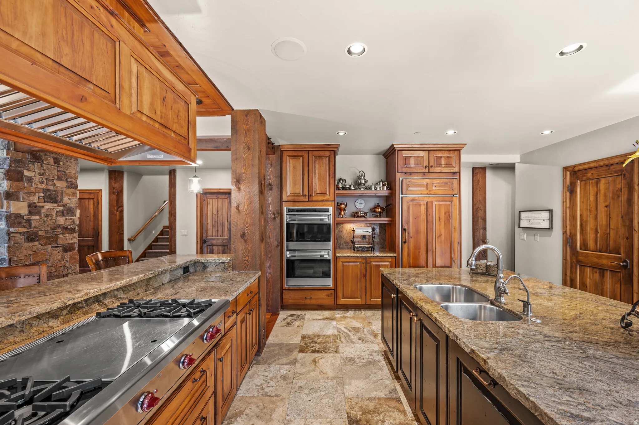 Kitchen featuring stainless steel appliances, wood finish cabinetry, dark stone counters, recessed lighting, and light stone finish flooring