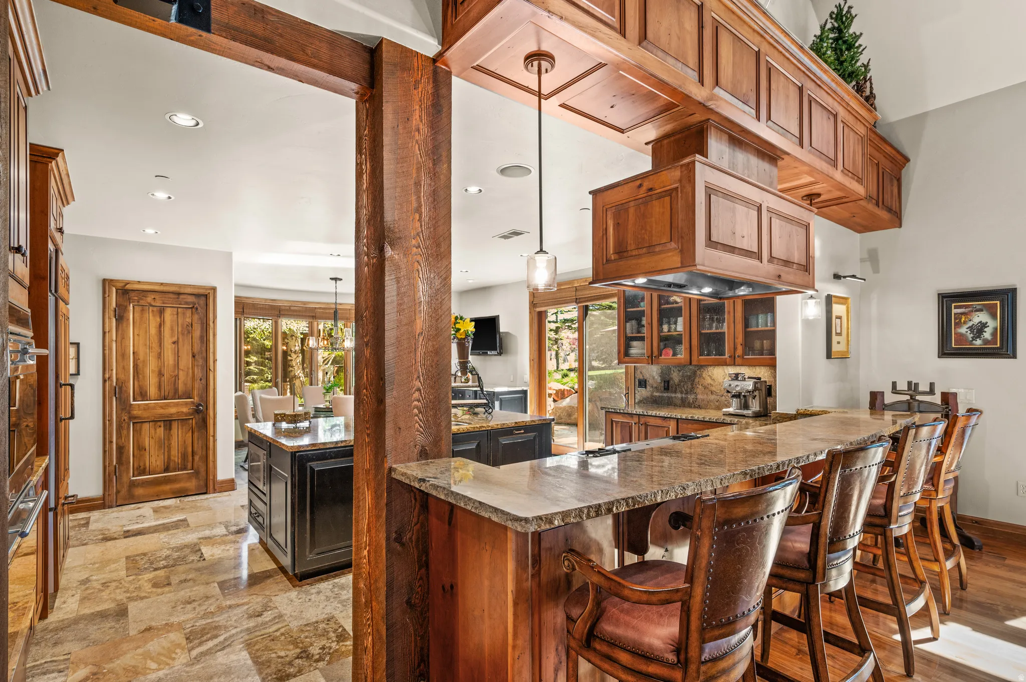 Bar area featuring decorative light fixtures, glass fronted cabinets, dark stone countertops, and healthy amount of natural light