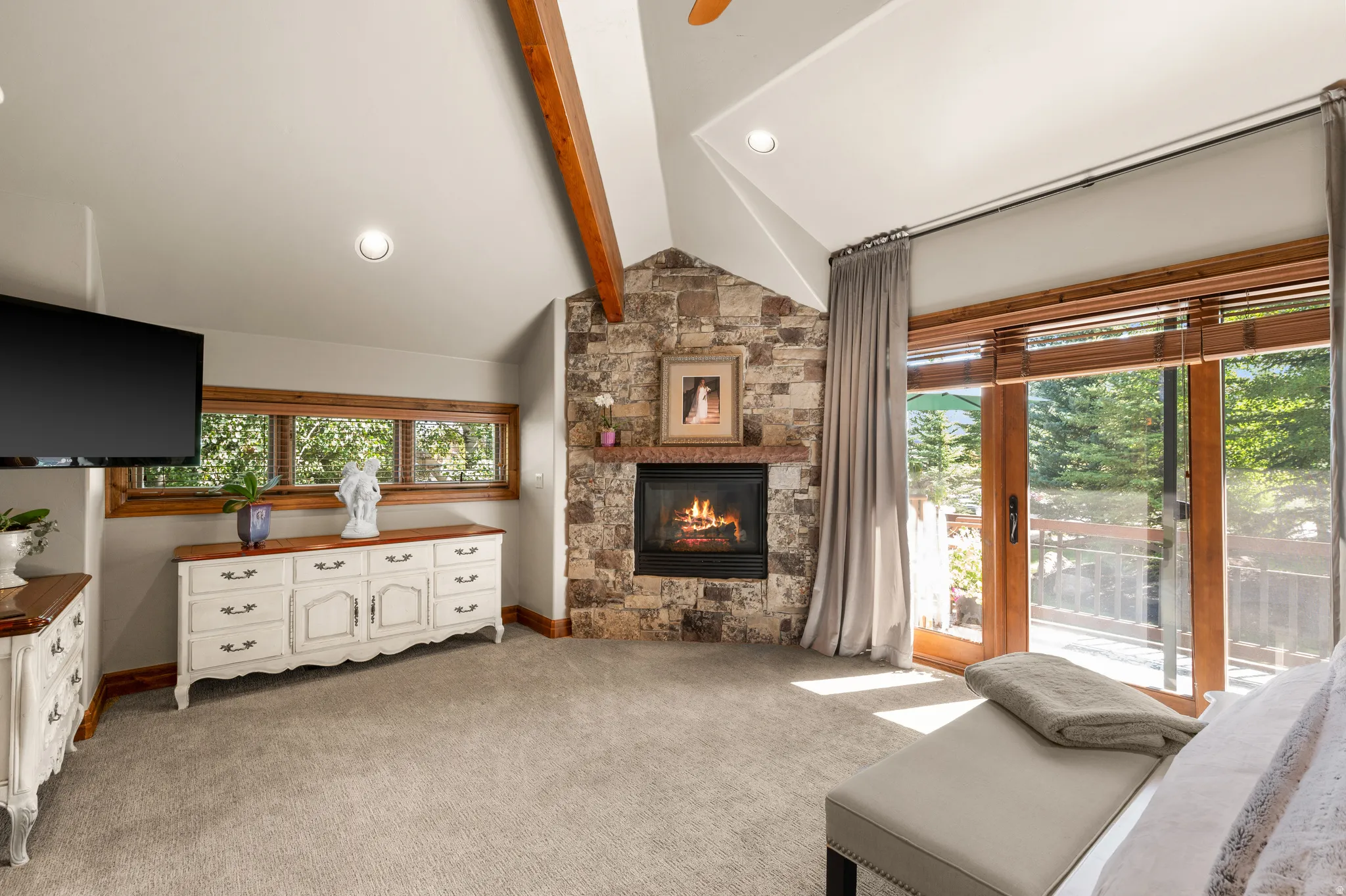 Living area with light colored carpet, a stone fireplace, and vaulted ceiling with beams