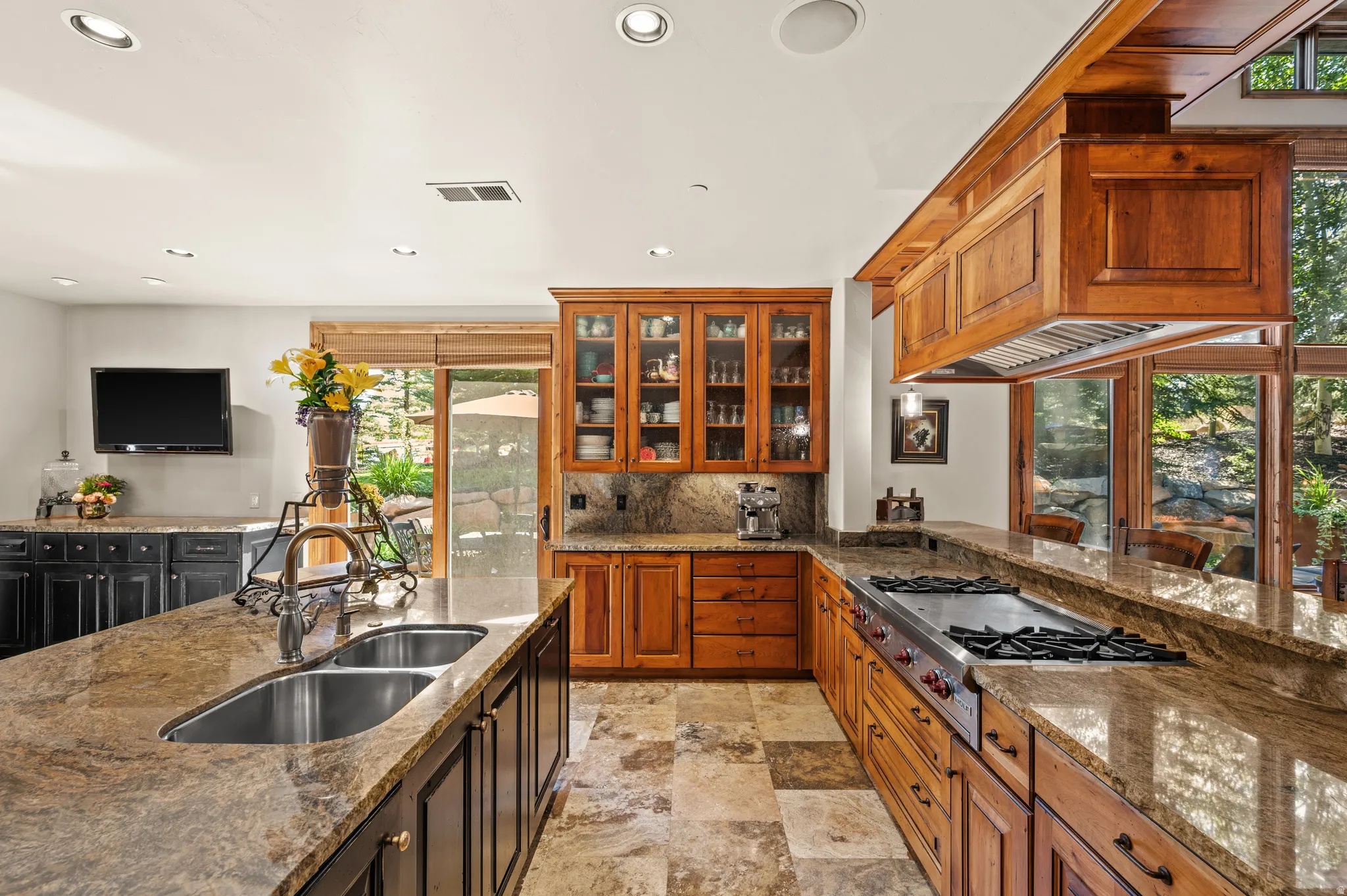 Kitchen featuring dark stone countertops, stainless steel gas cooktop, glass insert cabinets, light stone finish floors, and recessed lighting