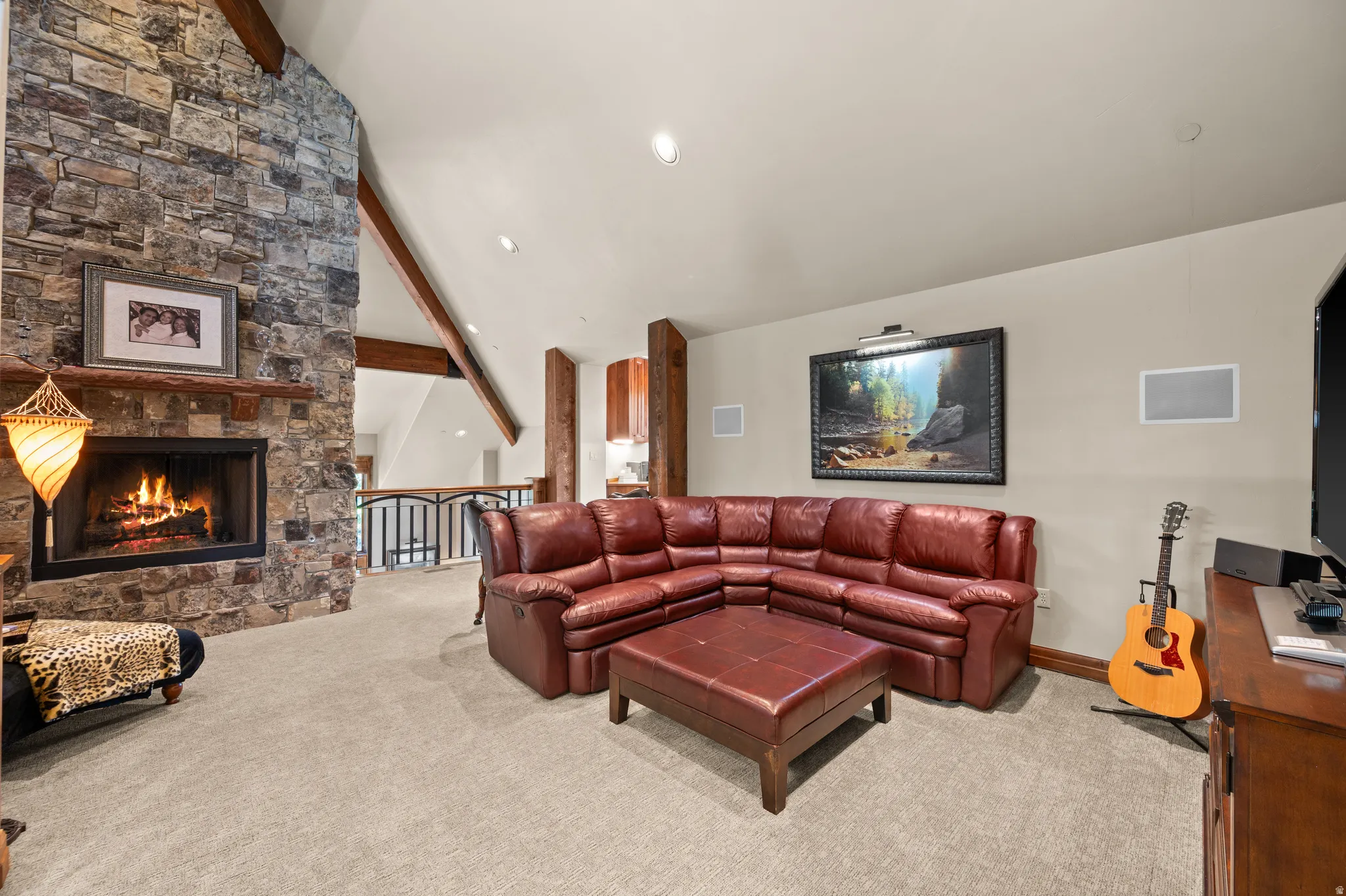 Living room with lofted ceiling with beams, light colored carpet, a stone fireplace, and recessed lighting