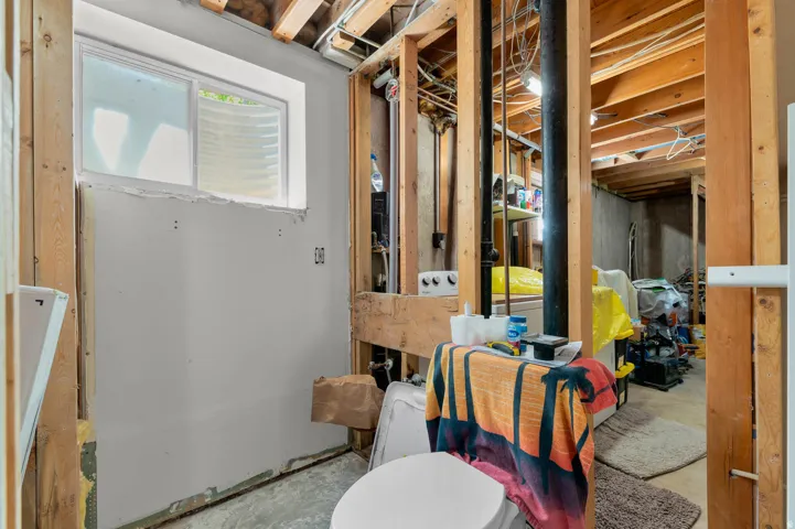 Basement area featuring exposed wood framing, an egress window, and a concrete floor