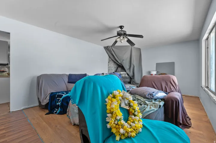 Living area featuring wood-finish flooring, a ceiling fan with integrated lighting, and natural light from a large window