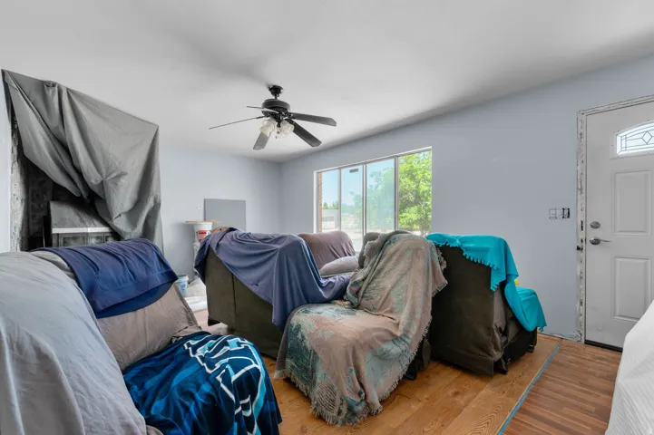 Living area featuring wood-finish flooring, a ceiling fan with integrated lighting, and multiple windows