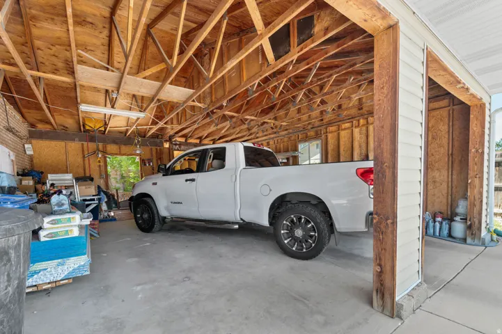 Open-air garage with exposed wood framing, concrete flooring, and a corrugated plastic roof
