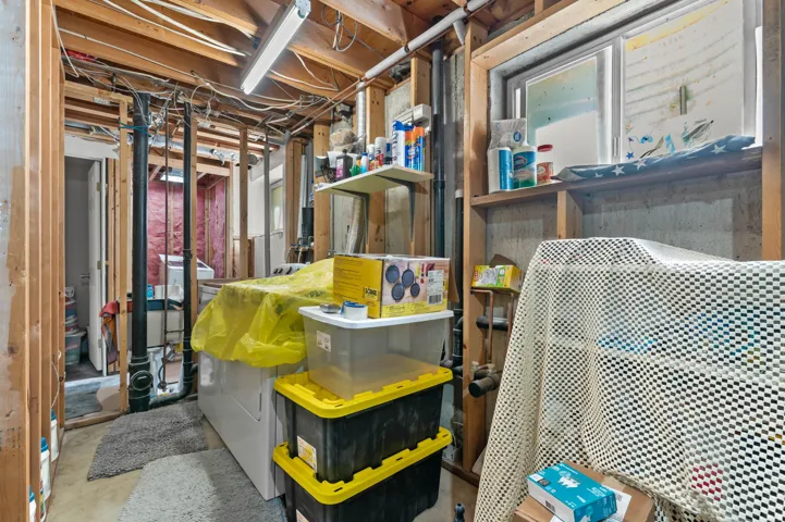 Basement utility area featuring exposed wood framing, concrete foundation walls, and visible plumbing and electrical infrastructure