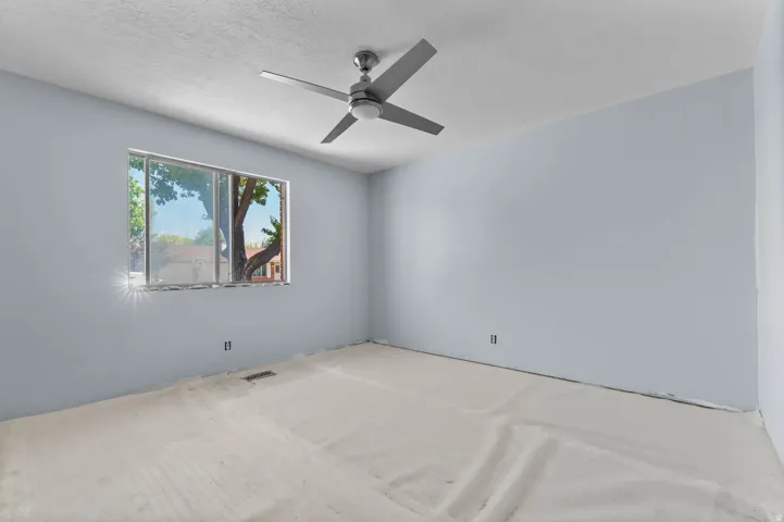 Room featuring a ceiling fan, a window with outdoor scenery, and light blue walls