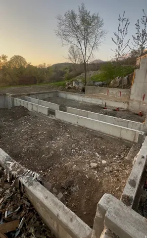 Concrete foundation footings with a tiered retaining wall, set against a backdrop of distant hills and mature trees