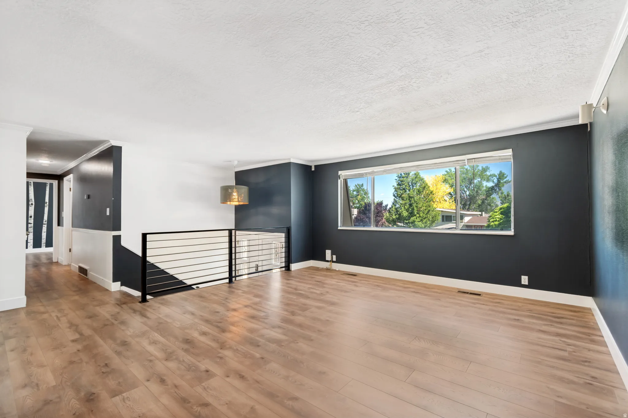 Bright living area featuring wood-finish flooring, a contemporary horizontal bar railing, a large picture window, and a modern drum pendant light fixture