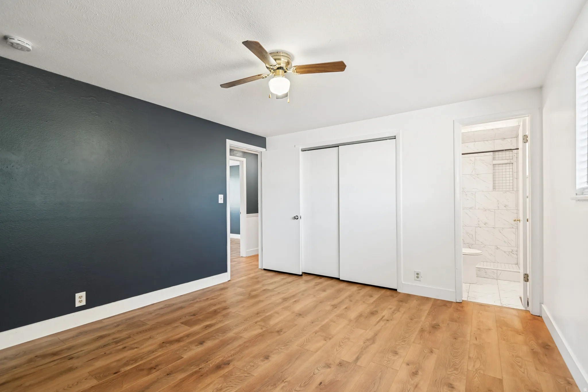 Spacious room featuring wood-finish flooring, a ceiling fan with integrated lighting, and a dark accent wall