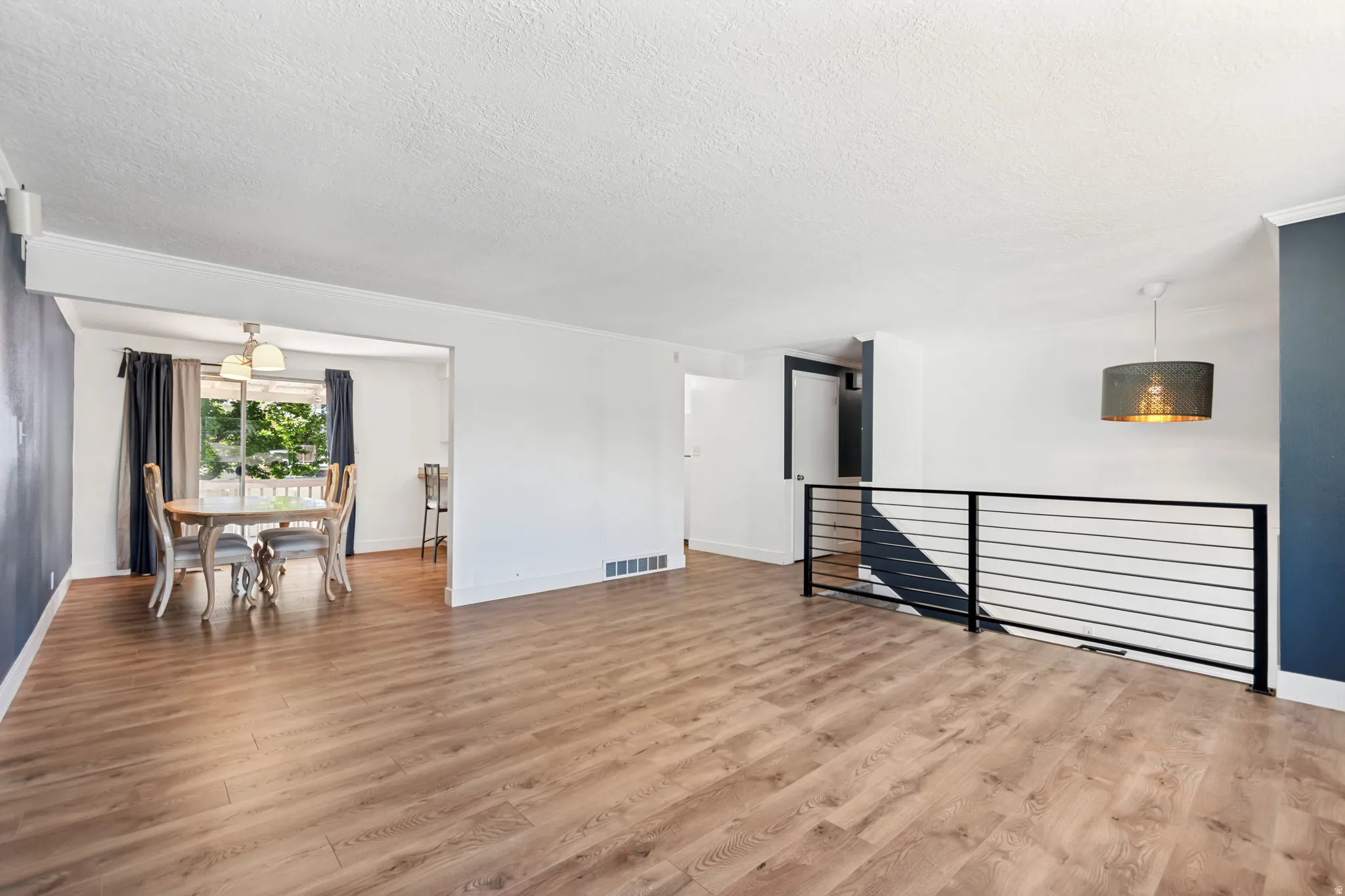 Expansive living area featuring wood-finish flooring, a contemporary black horizontal bar railing, and a modern drum pendant light fixture