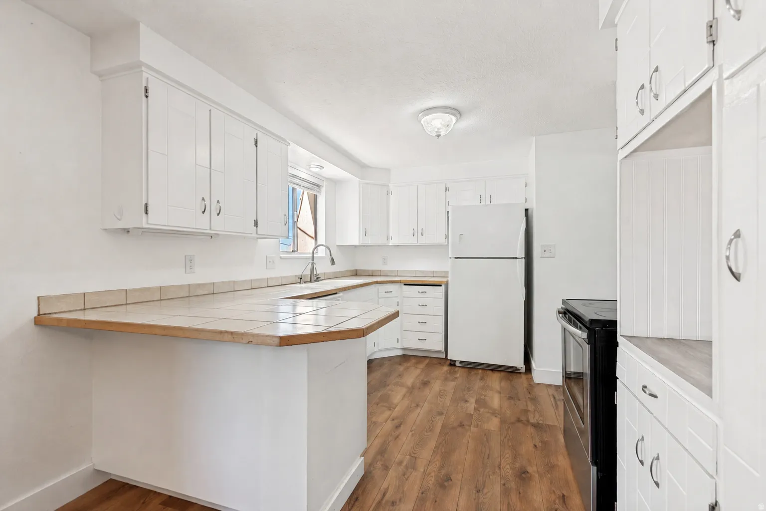 Kitchen featuring extensive white cabinetry, wood-finish flooring, and a peninsula with a tile countertop