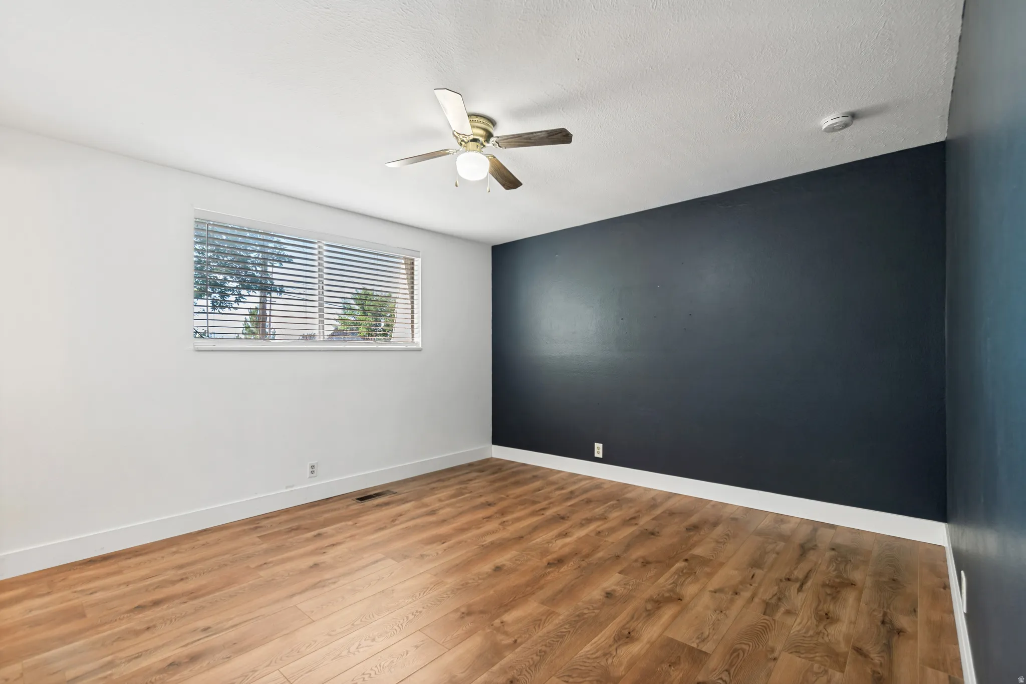 Room featuring wood-finish flooring, a ceiling fan with integrated lighting, and a window with horizontal blinds