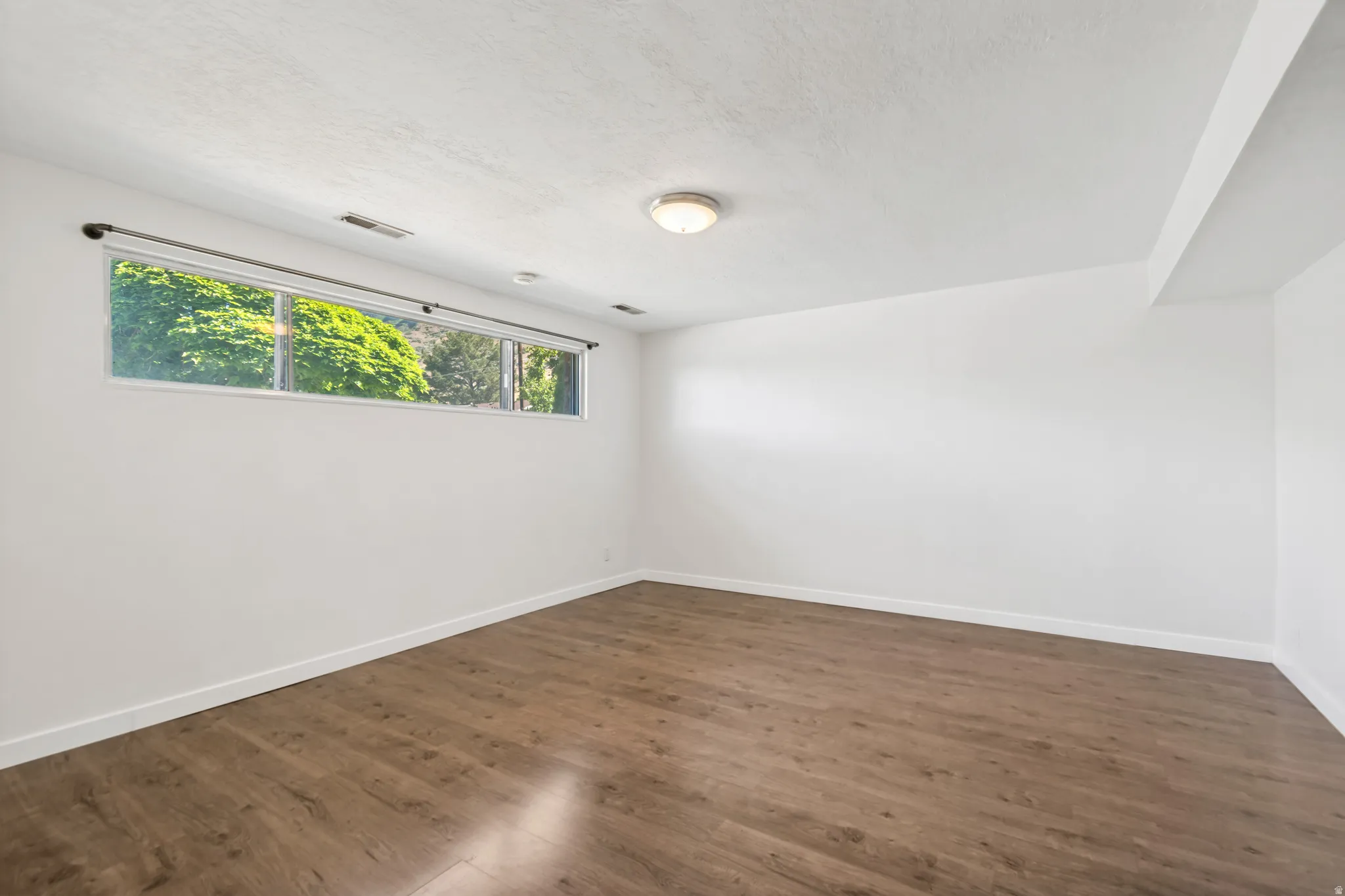 Spacious room featuring daylight window, wood-finish flooring and a neutral color palette