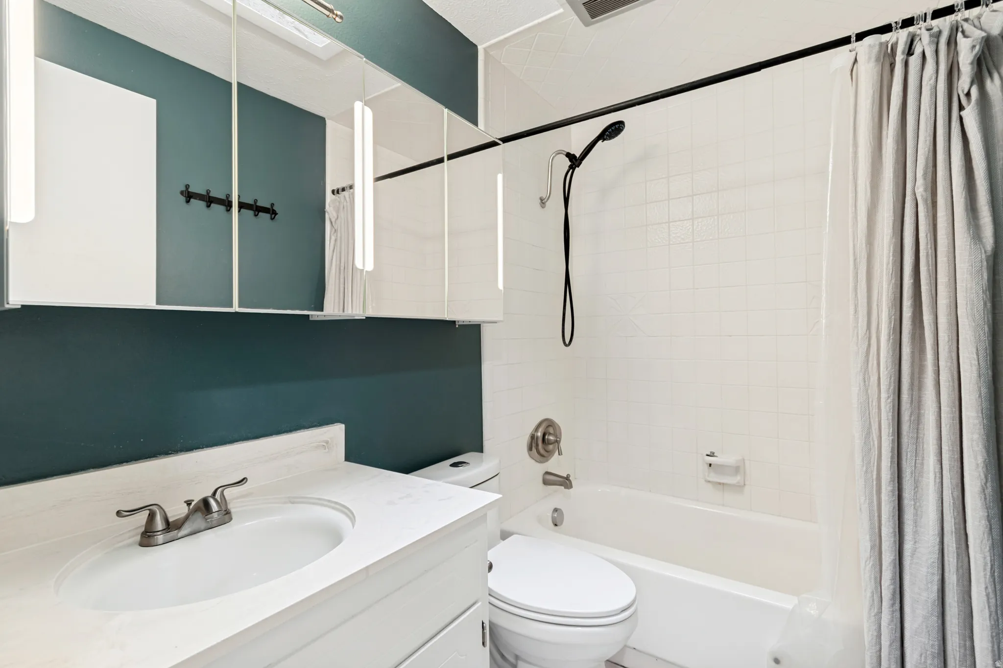 Bathroom vanity with an integrated sink and brushed nickel faucet, complemented by a large mirrored medicine cabinet, &  sky light