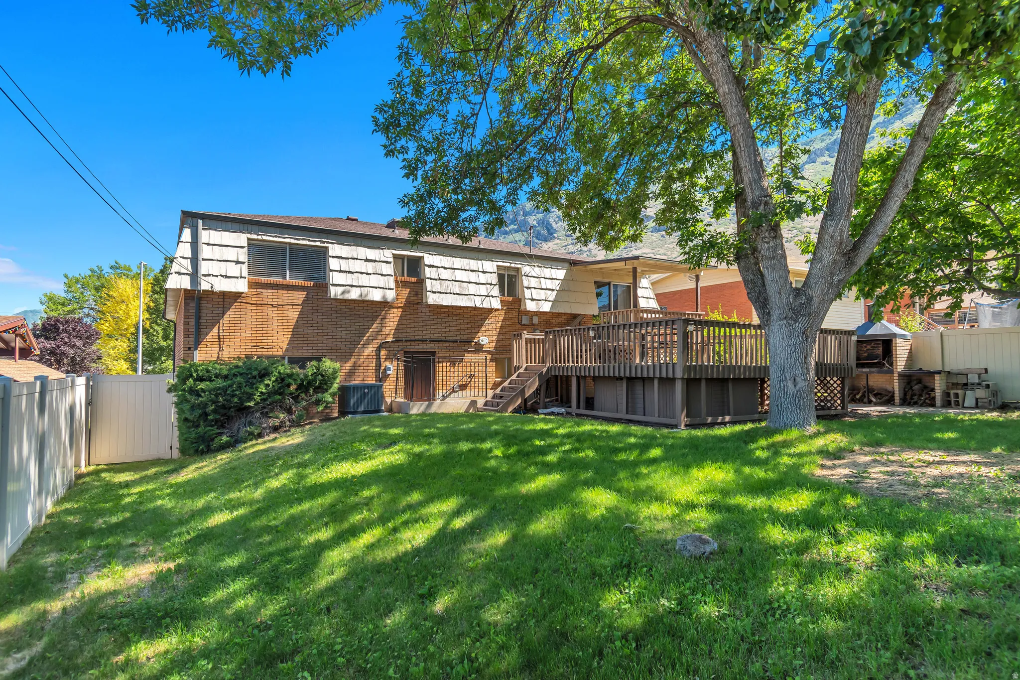 Expansive backyard featuring a manicured lawn, mature shade tree, and wood-finish decking