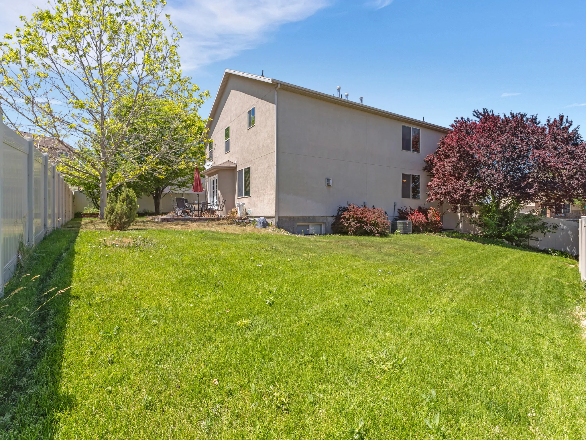 Expansive backyard featuring a large grass lawn, mature trees, and a concrete patio