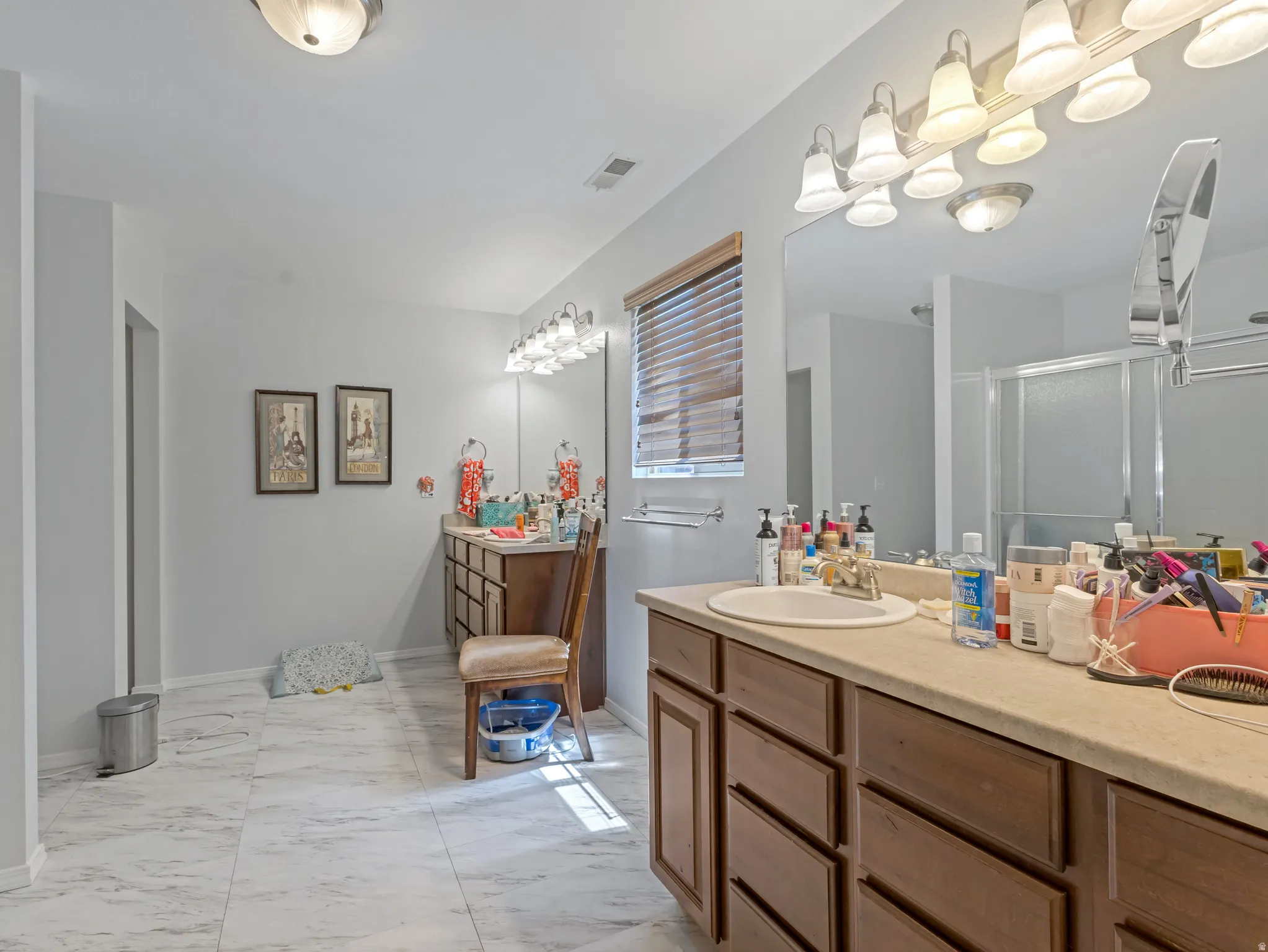 Expansive bathroom featuring wood-finish vanity cabinetry with an integrated sink, a large wall-mounted mirror, overhead lighting, and white tile flooring