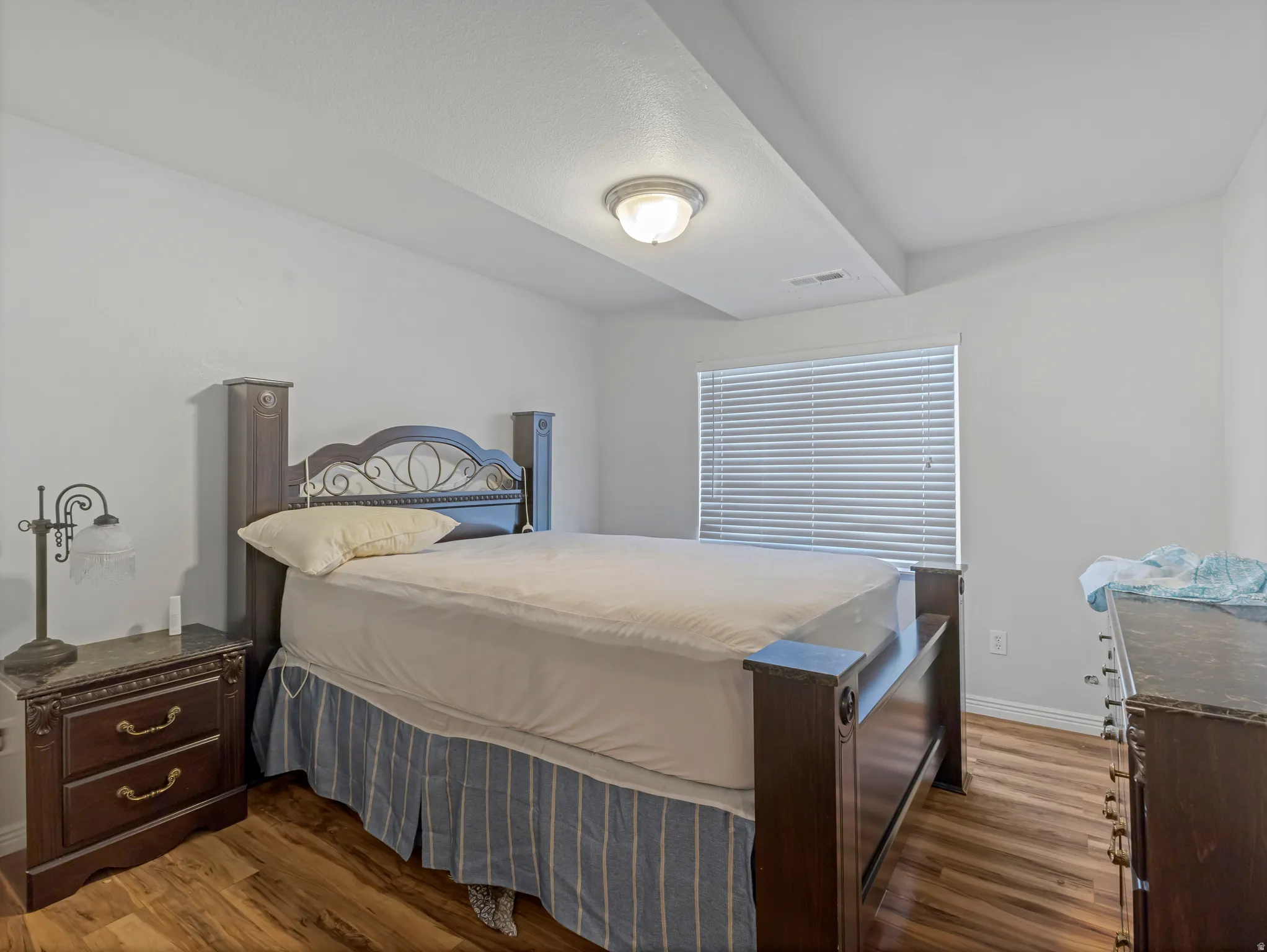Bedroom featuring wood-finish flooring, a neutral color palette, and a window with horizontal blinds