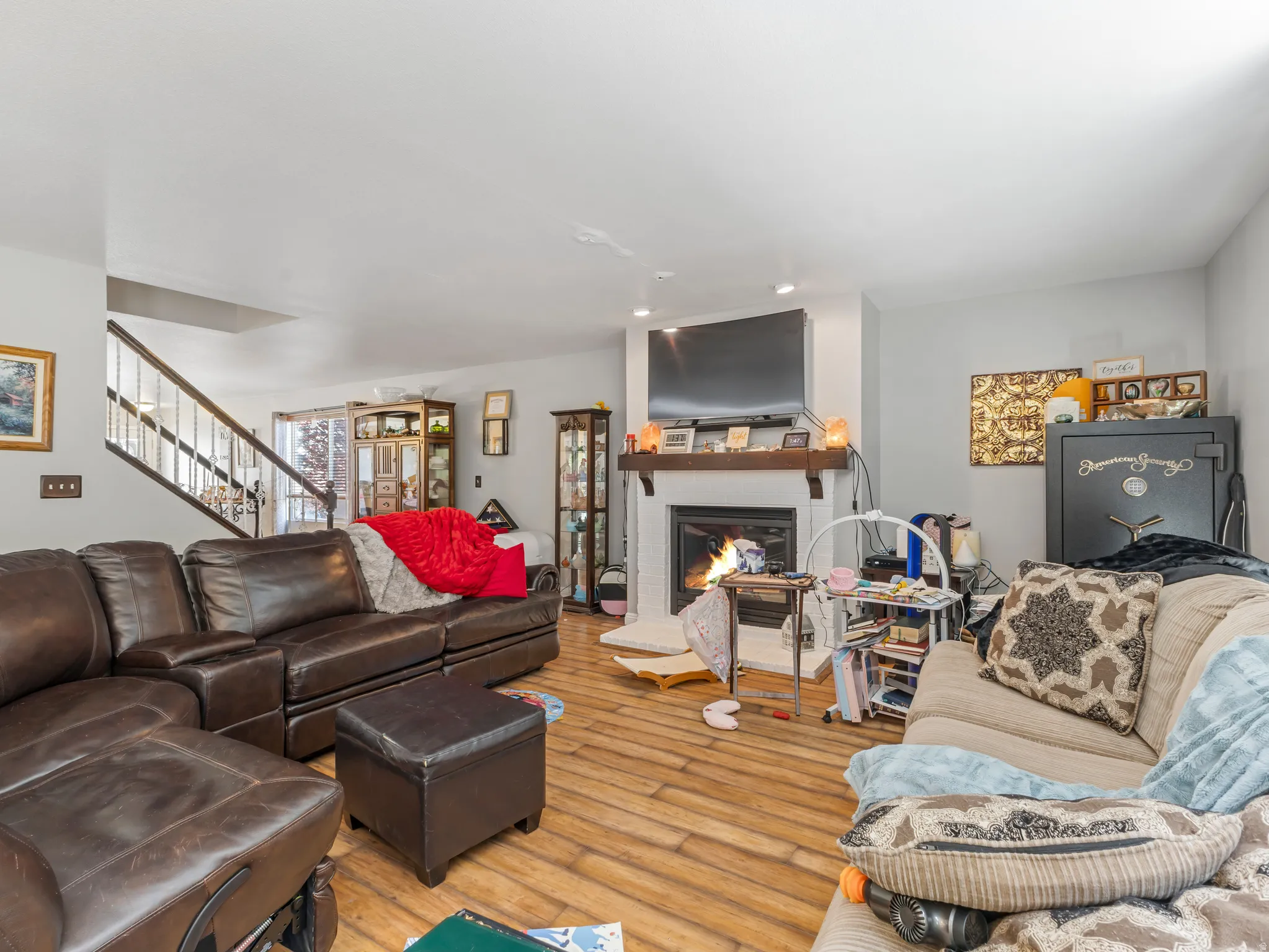 Living area featuring wood-finish flooring, a white brick fireplace with a wood mantle, and a staircase with a wood handrail