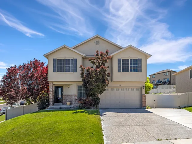 Two-story residence featuring a light-colored stucco exterior with brick accents, an attached two-car garage, and a concrete driveway
