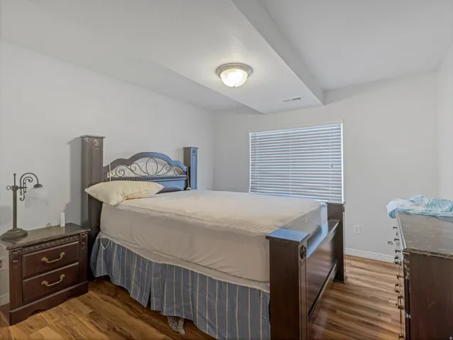 Bedroom featuring wood-finish flooring, a neutral color palette, and a window with horizontal blinds