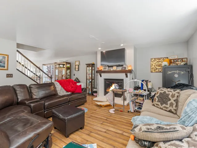 Living area featuring wood-finish flooring, a white brick fireplace with a wood mantle, and a staircase with a wood handrail