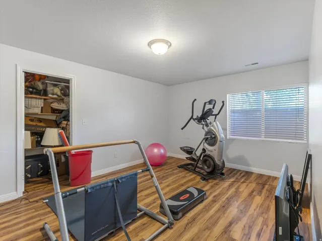 Bright room featuring wood-finish flooring, a flush-mount ceiling light, white walls, and a window with horizontal blinds