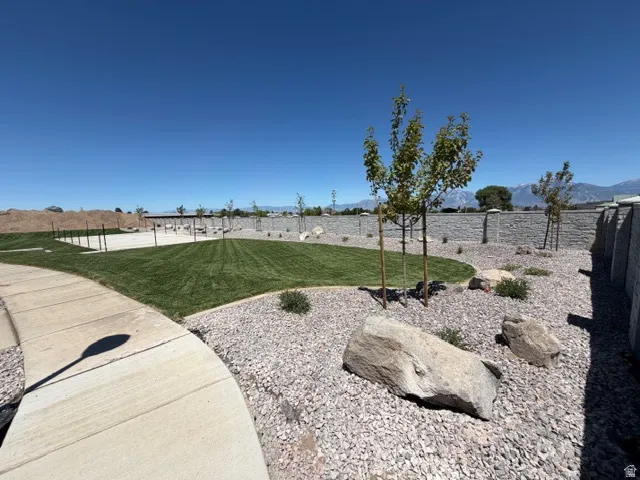 Expansive green space featuring a curved concrete pathway, a manicured lawn, and low-maintenance rock landscaping with mature trees and large boulders
