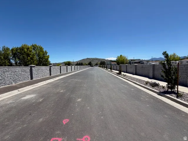 Paved street with concrete curbing and sidewalks, bordered by a stone-faced privacy wall with decorative pillar caps