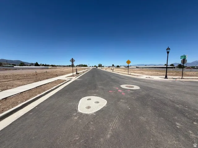 Newly paved asphalt road featuring concrete sidewalks, street lamps, and street signage