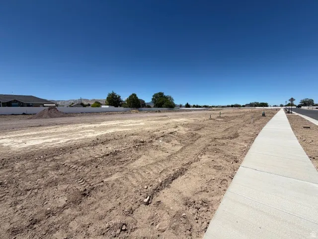 Expansive cleared lot featuring a new concrete sidewalk, established roadway, and distant mountain backdrop
