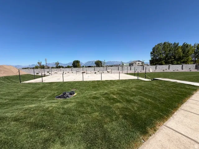 Expansive green lawn featuring a concrete patio base, a concrete walkway, and a stone-clad perimeter wall