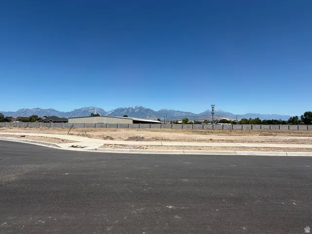 Expansive undeveloped lot with paved road frontage, concrete sidewalk, and a distant mountain backdrop
